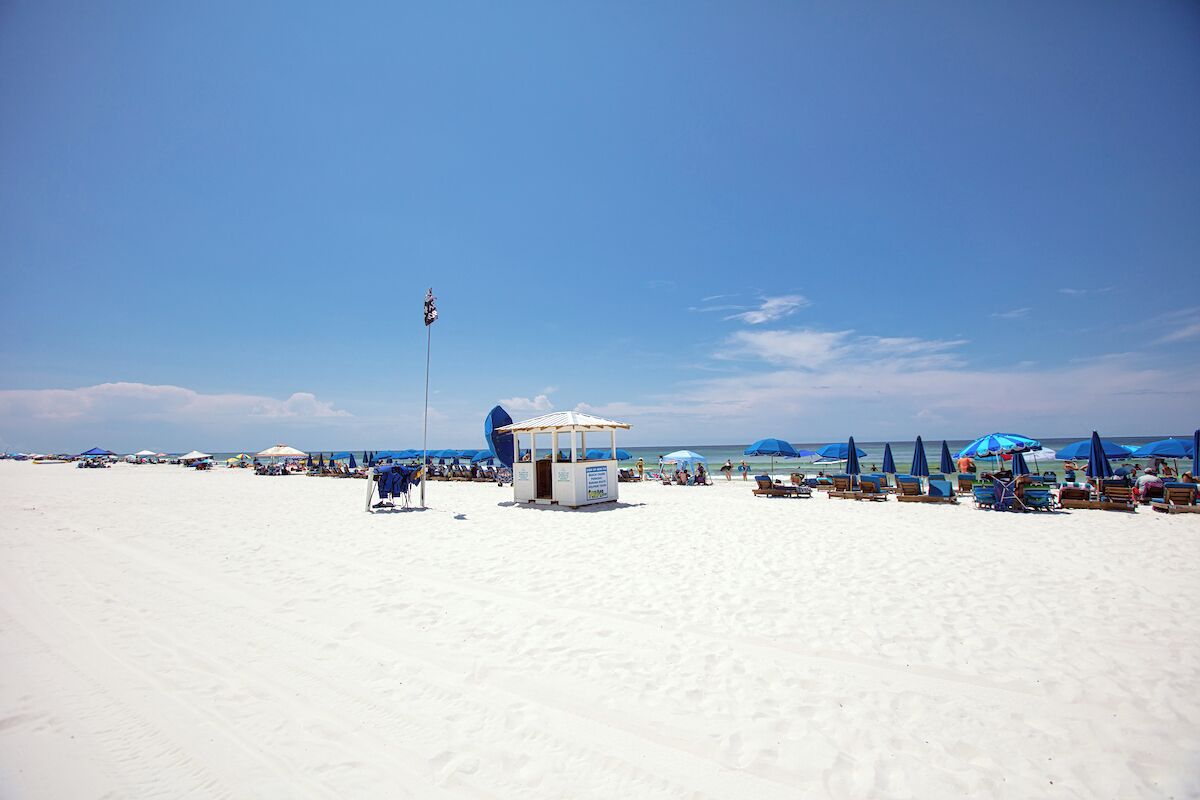 A beach with white sand, blue umbrellas, and a small kiosk.