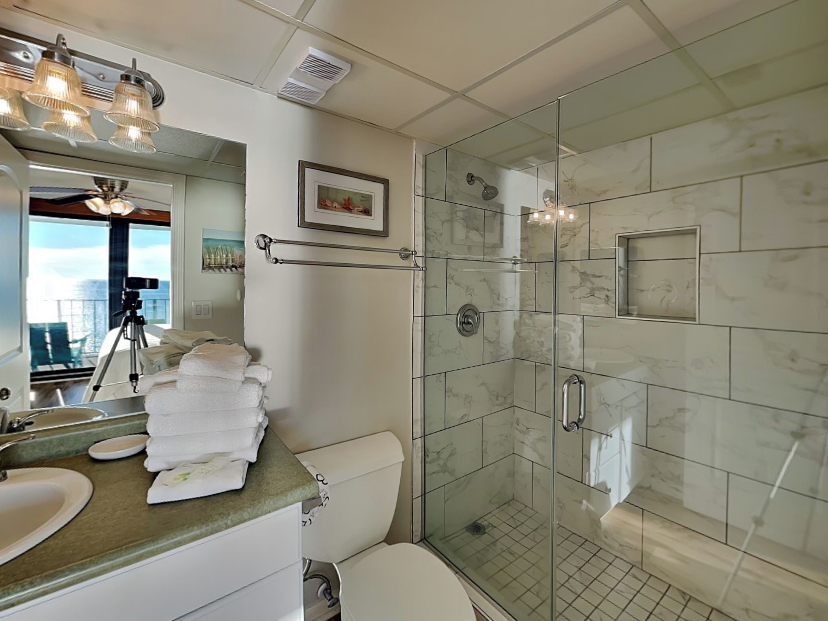 Une salle de bain moderne avec une douche à parois de verre, un meuble-lavabo avec un évier et un miroir, et un tableau encadré accroché au mur.