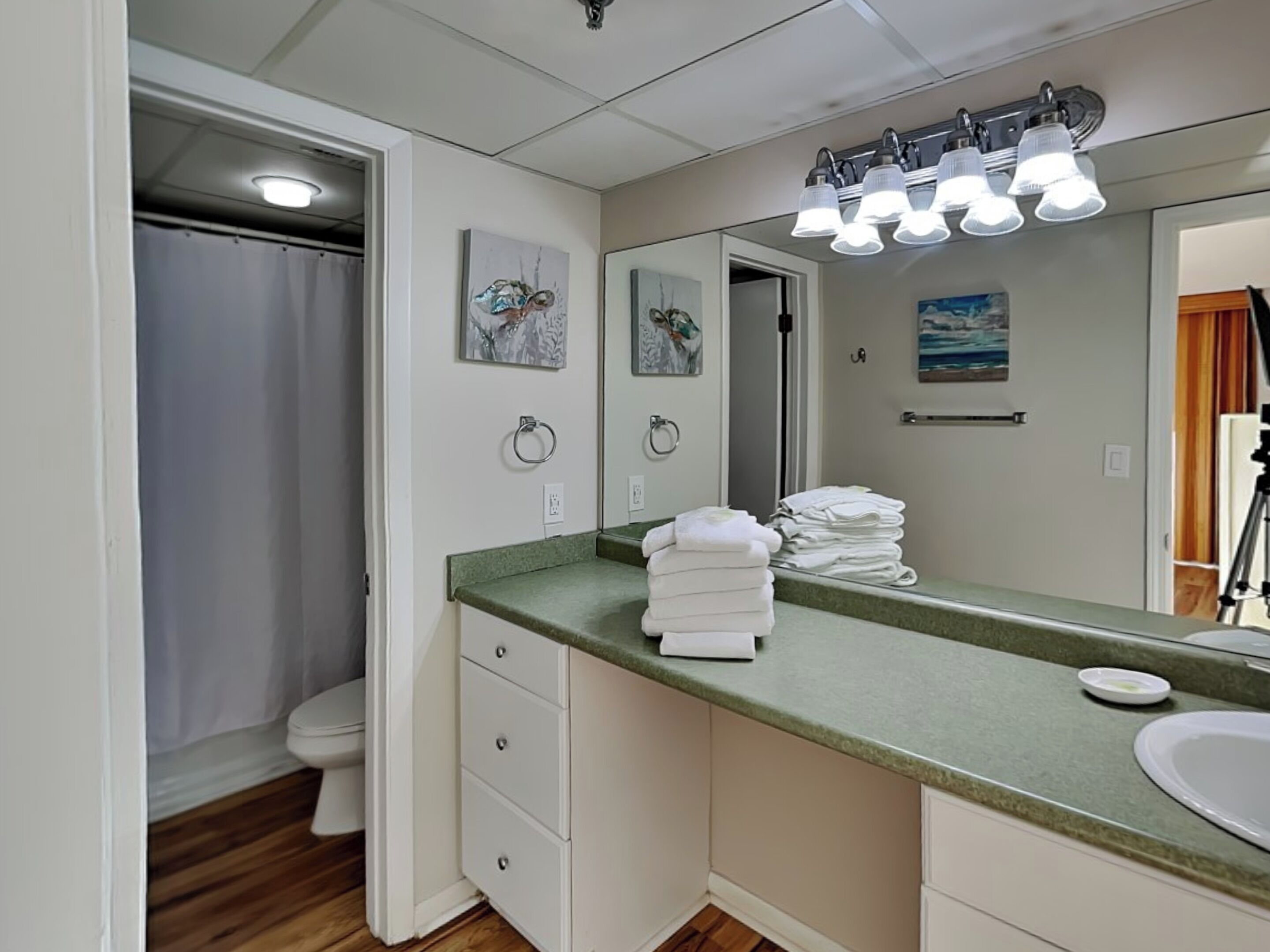 Un bagno con un piano d'appoggio verde, lavandino bianco e uno specchio. Asciugamani sono impilati sul piano e si vede una tenda della doccia sullo sfondo.