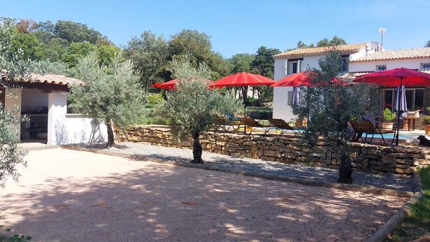 A villa with a stone wall, outdoor seating, and red umbrellas. - Location à la Semaine (Néoules)