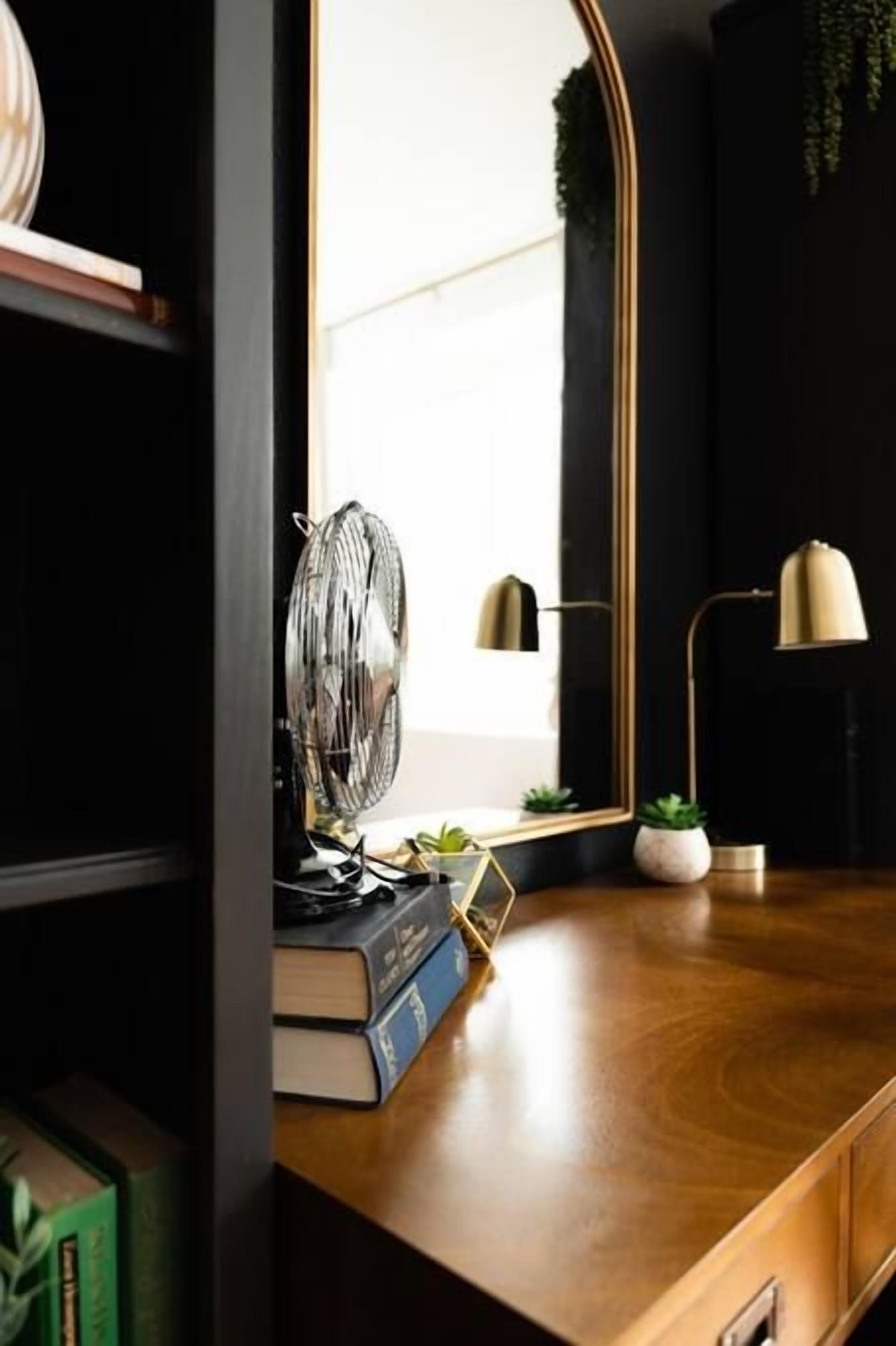 A wooden desk with a mirror, a fan, a lamp, and some books.