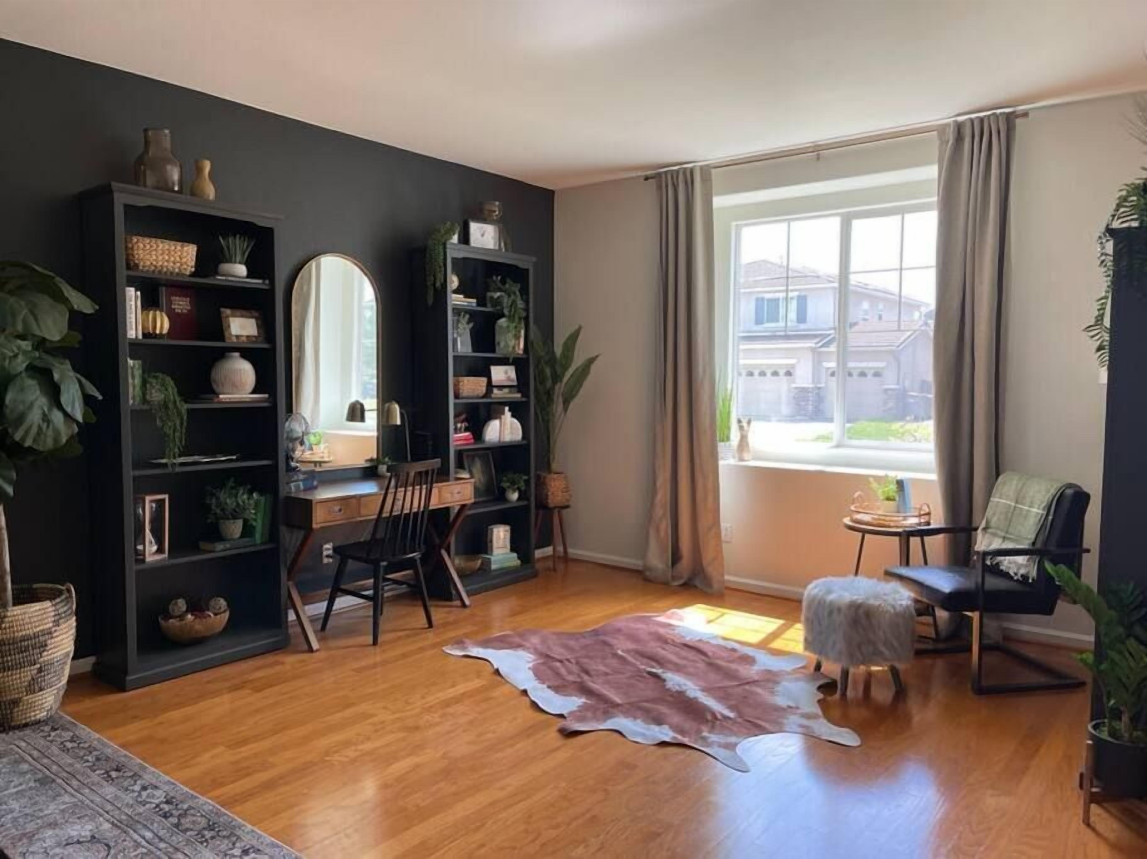 Ein Zimmer mit Holzboden, einem Lederteppich, einem Schreibtisch mit Stuhl, einem Bücherregal und einem Fenster mit Vorhängen.