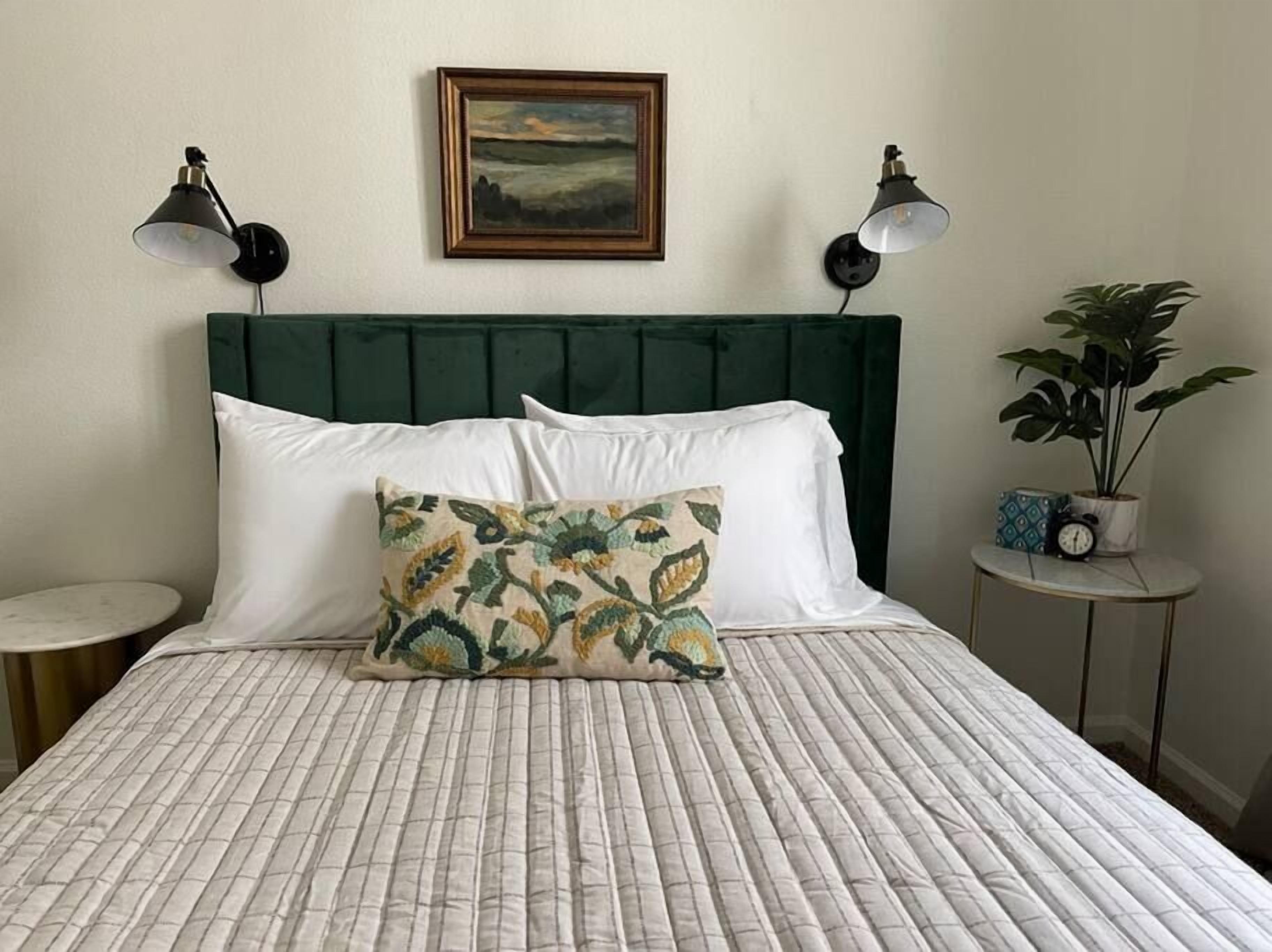 Een bed met een gewatteerd patroon, een groen gestoffeerd hoofdbord en twee bedlampen.