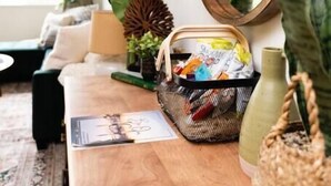 Een houten tafel met een mand lekkernijen, een kleine plant in een pot en een spiegel.