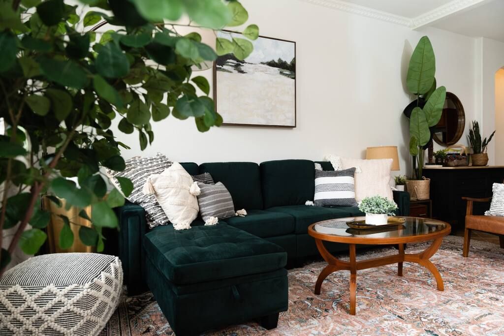 Un salon avec un canapé vert foncé, une table basse ronde et un tapis à motifs.