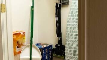 Een smalle gang met een bezem, blik en schoonmaakspullen.