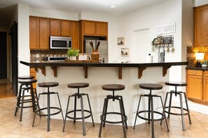 A kitchen with wooden cabinets, a central island with stools, a microwave, and a refrigerator.