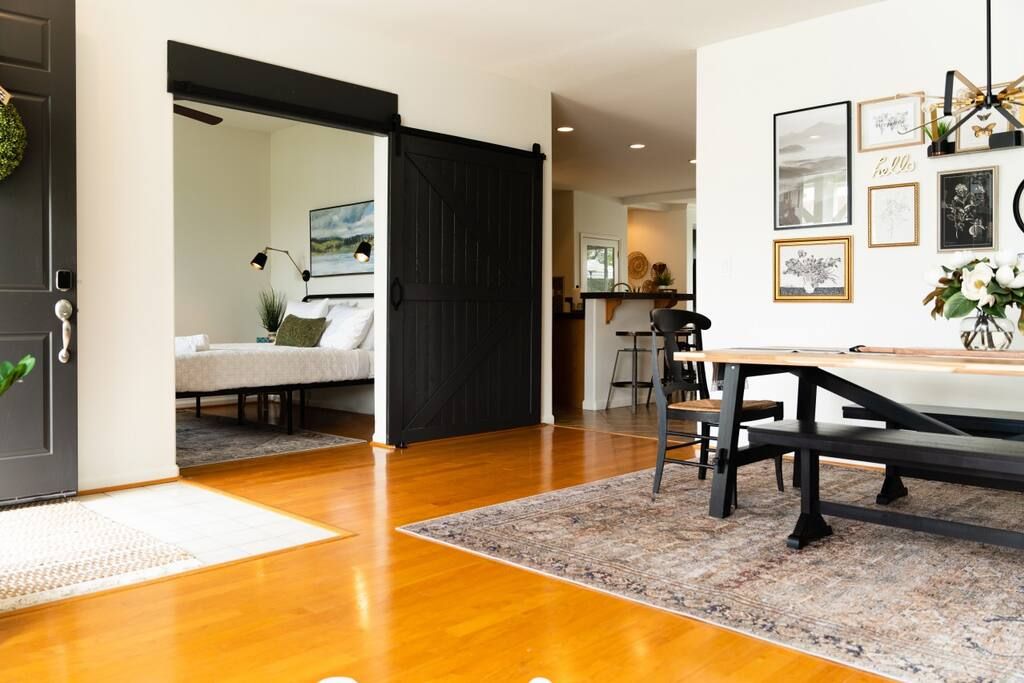 Une pièce avec un plancher en bois, une table à manger avec des chaises, une porte coulissante noire et un mur orné de tableaux encadrés.