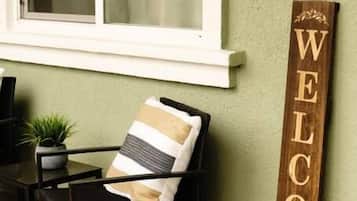 Una silla de metal negro con un cojín a rayas, un letrero de madera con la palabra 'WELCOME' grabada, y una pequeña planta en maceta sobre una mesa.