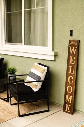 Une chaise en métal noir avec un coussin à rayures, une enseigne en bois sur laquelle est gravé le mot « BIENVENUE », et une petite plante en pot posée sur une table.