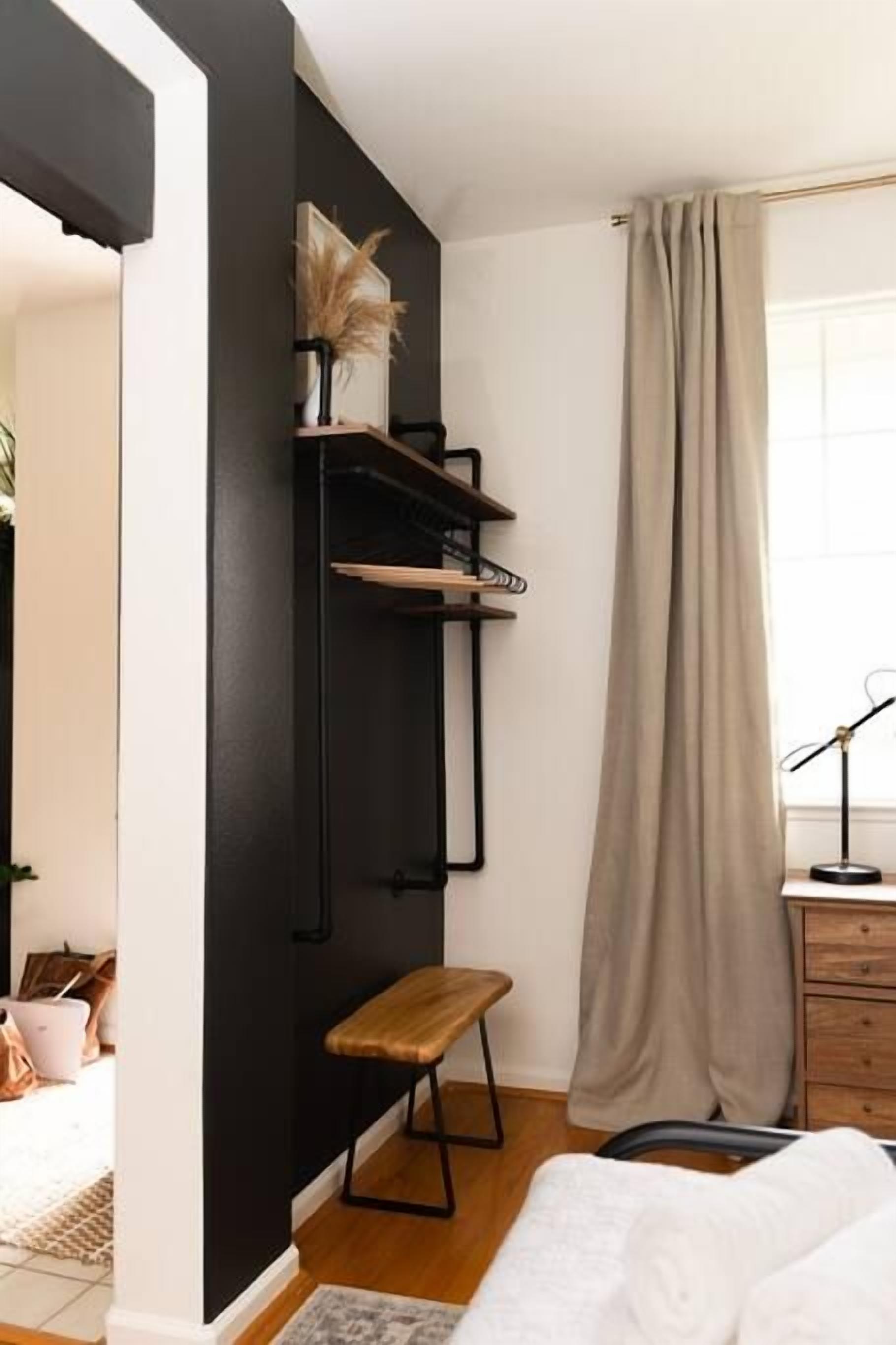Une chambre à coucher avec un lit, un banc, un bureau avec une lampe et une fenêtre avec un rideau.