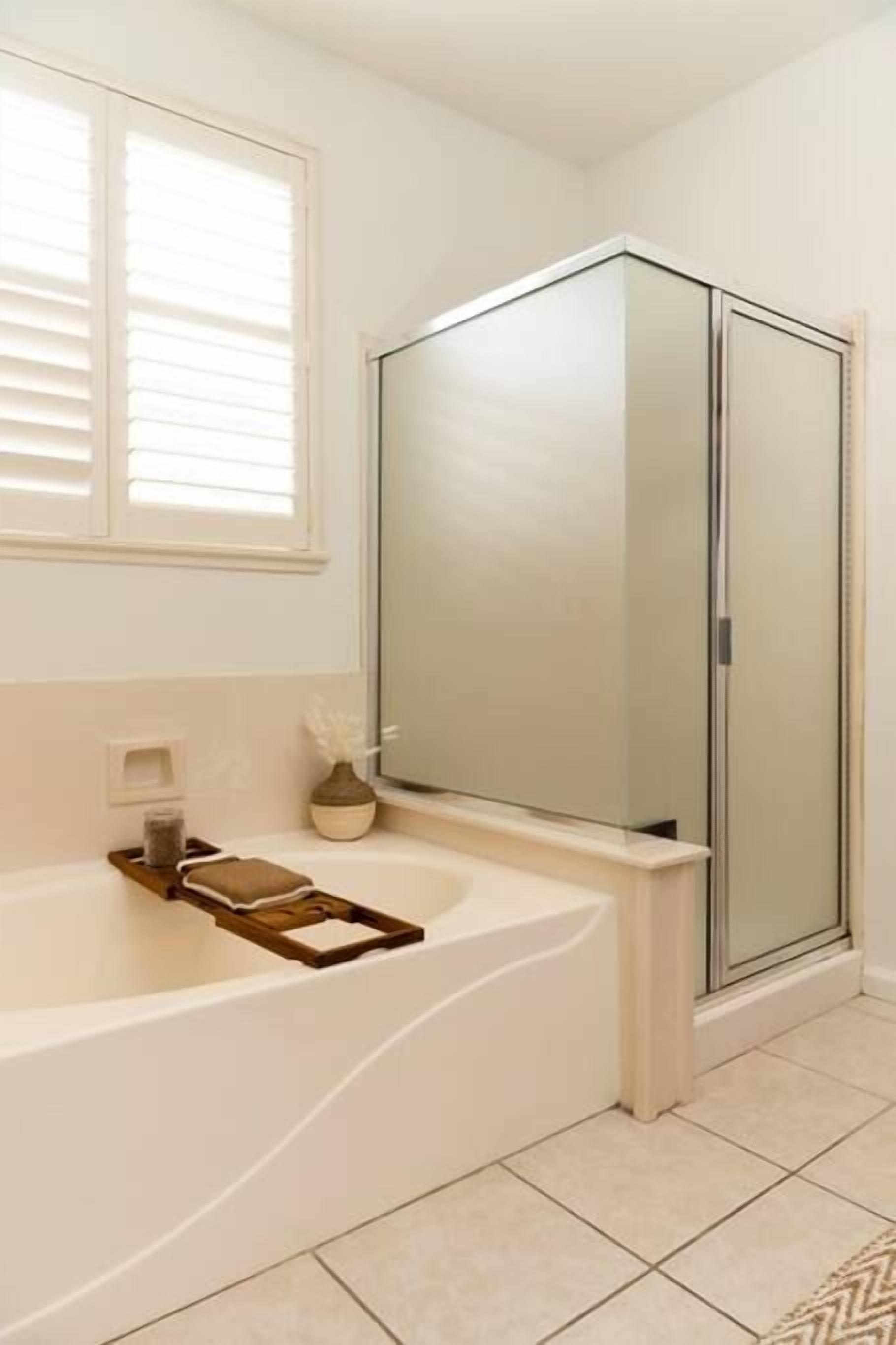 Un baño con bañera, cabina de ducha de vidrio y ventana con persianas.