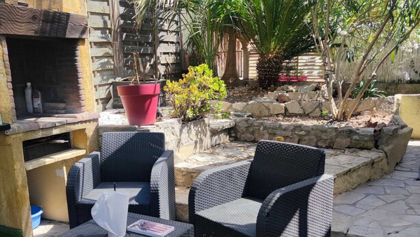 Un'area patio all'aperto con mobili in vimini, un barbecue e piante in vaso.