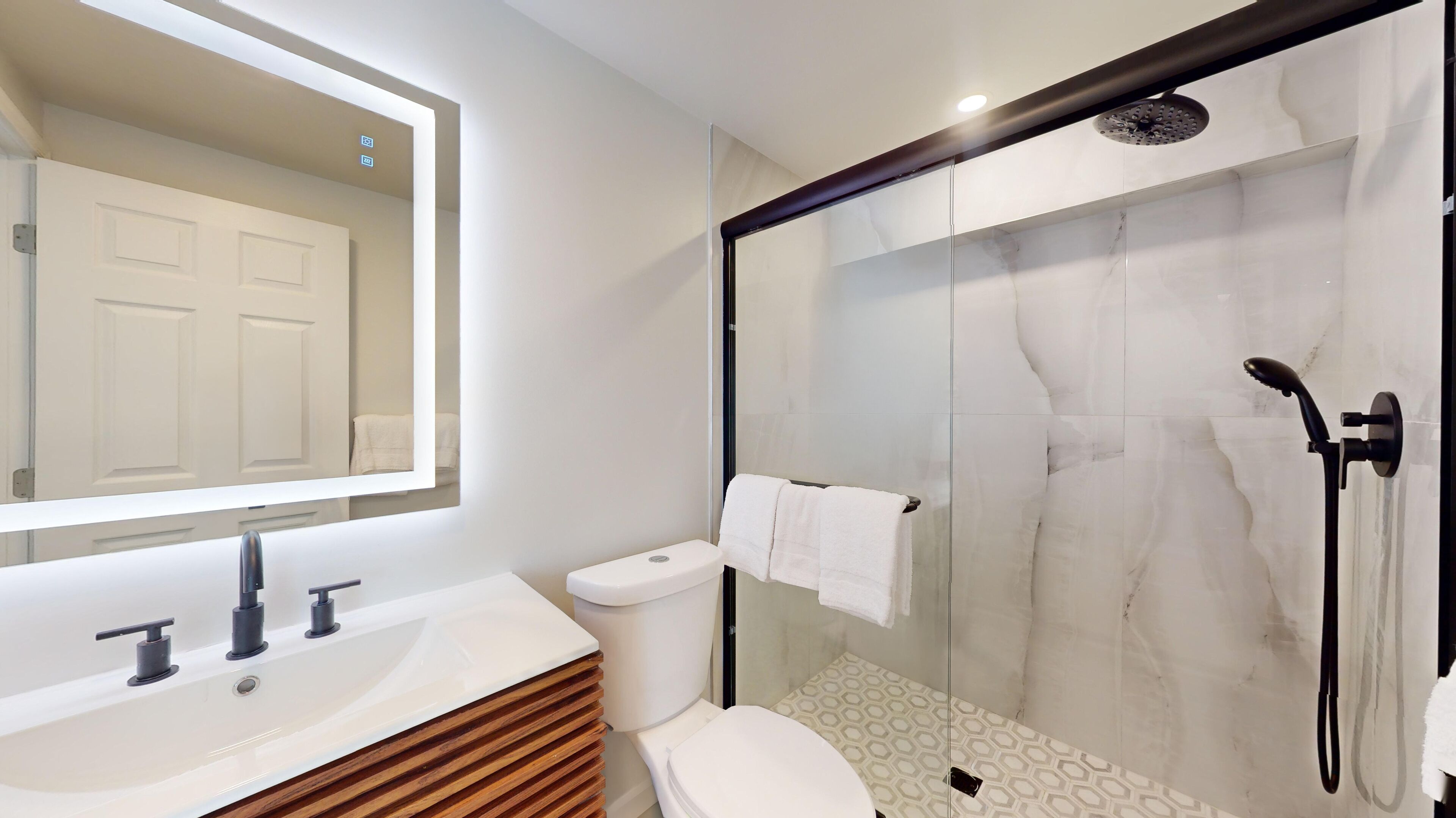 Un bagno moderno con cabina doccia in vetro, un lavandino bianco con mobile in legno e uno specchio grande.