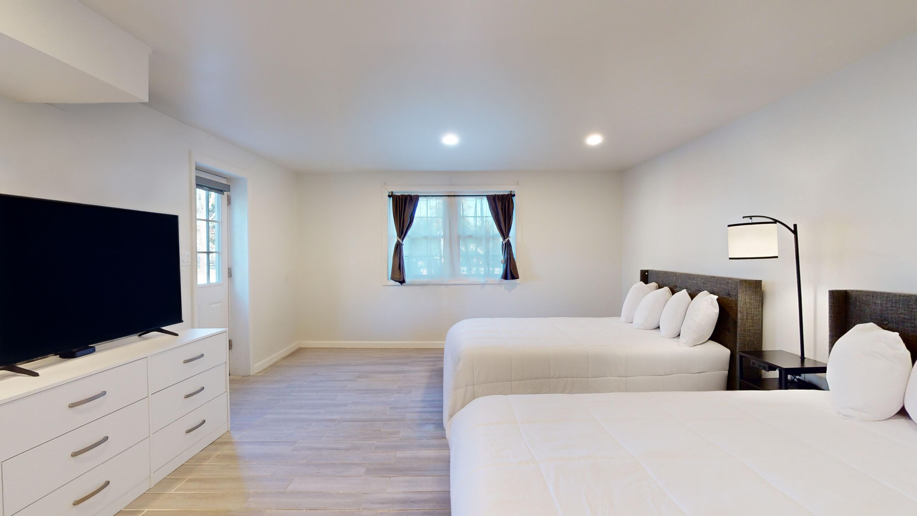 Habitación de hotel con televisión de pantalla plana, cómoda, dos camas, ventana con cortinas y lámpara de noche.