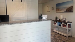 A reception desk with a white and black color scheme, a mounted TV, and a framed painting on the wall. - The Cape (Cape May)