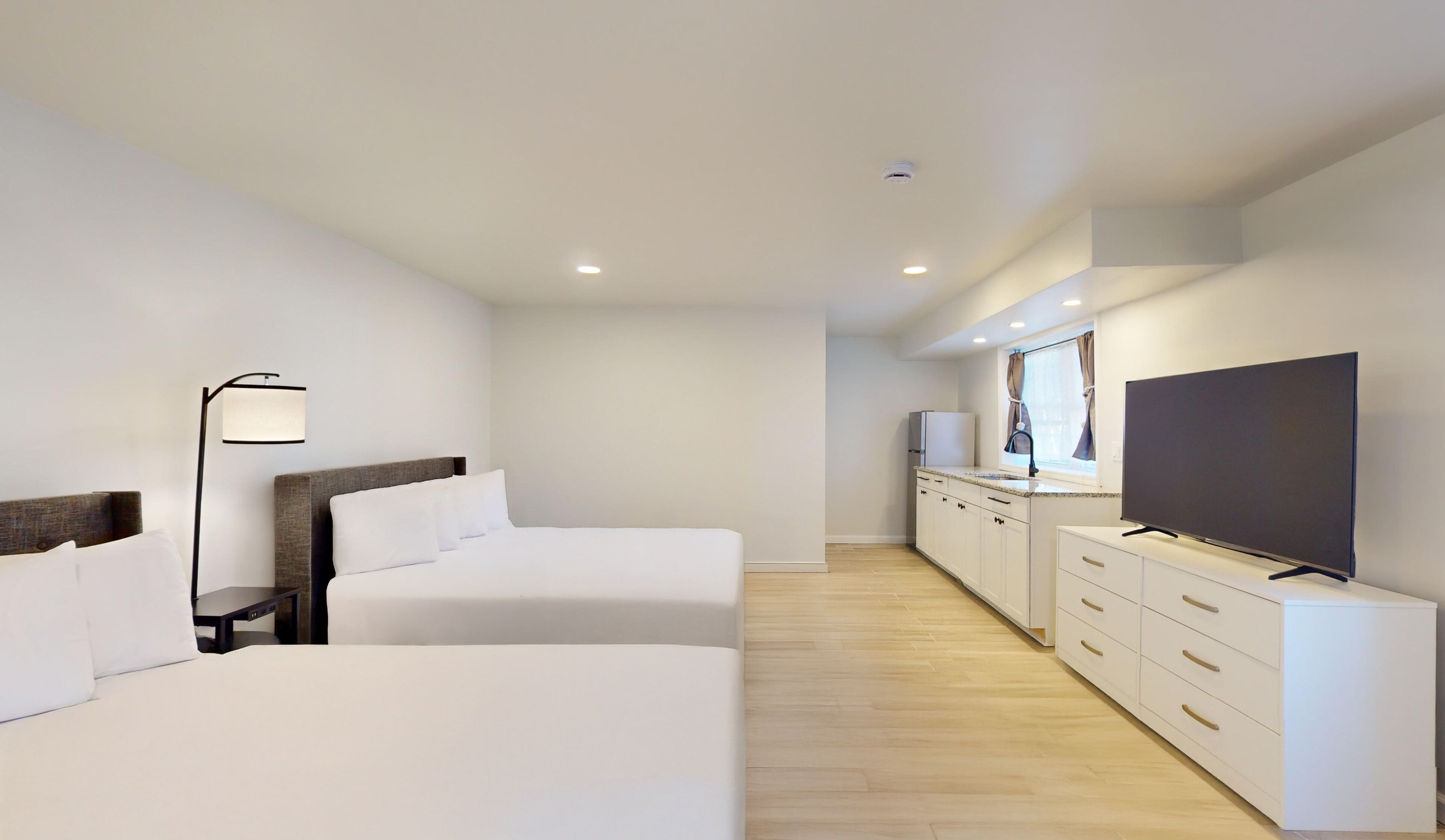 Une chambre d’hôtel moderne équipée de deux lits, d’une télévision, d’une kitchenette et d’une salle de bain.
