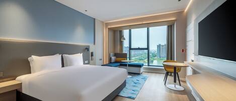 A modern hotel room with a large bed, a desk, a chair, and a view of the city.