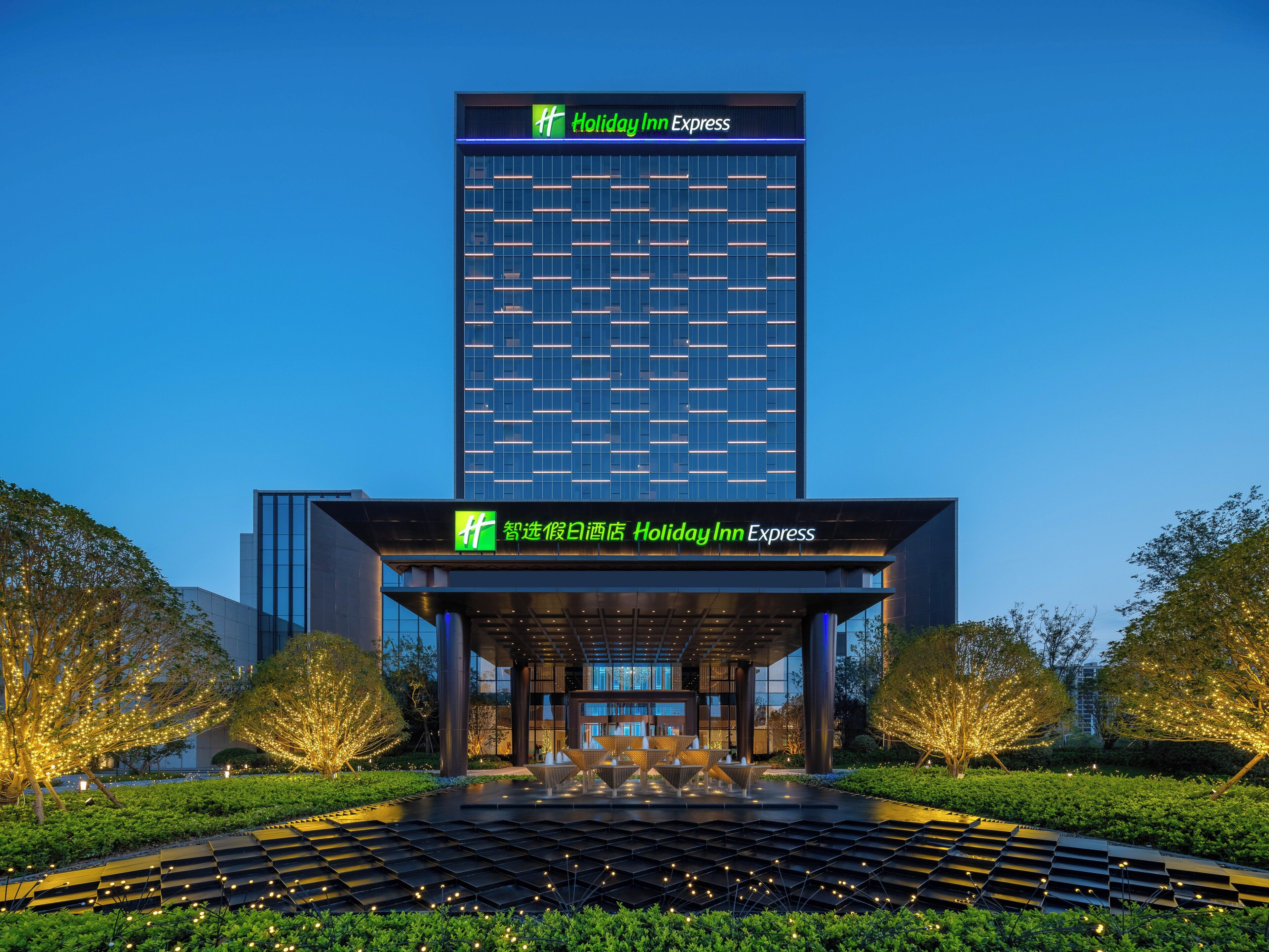 A Holiday Inn Express hotel with a modern glass facade, a covered entrance, and a landscaped garden area.