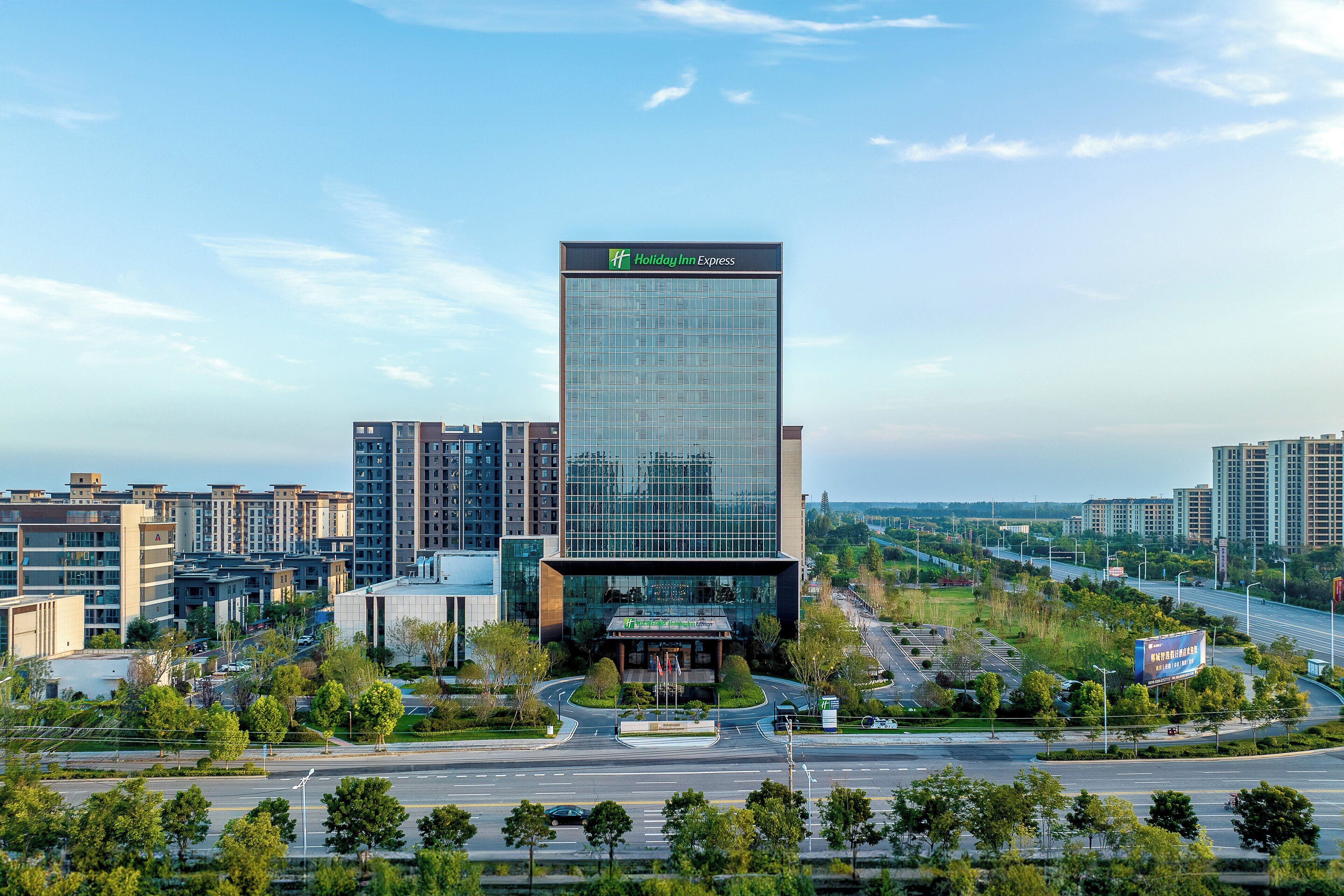 A modern hotel with a glass facade, surrounded by urban buildings and a clear sky.