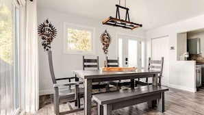 Un espace repas moderne avec une table rectangulaire, six chaises et un banc. Des œuvres d’art décoratives ornent les murs au-dessus des fenêtres.