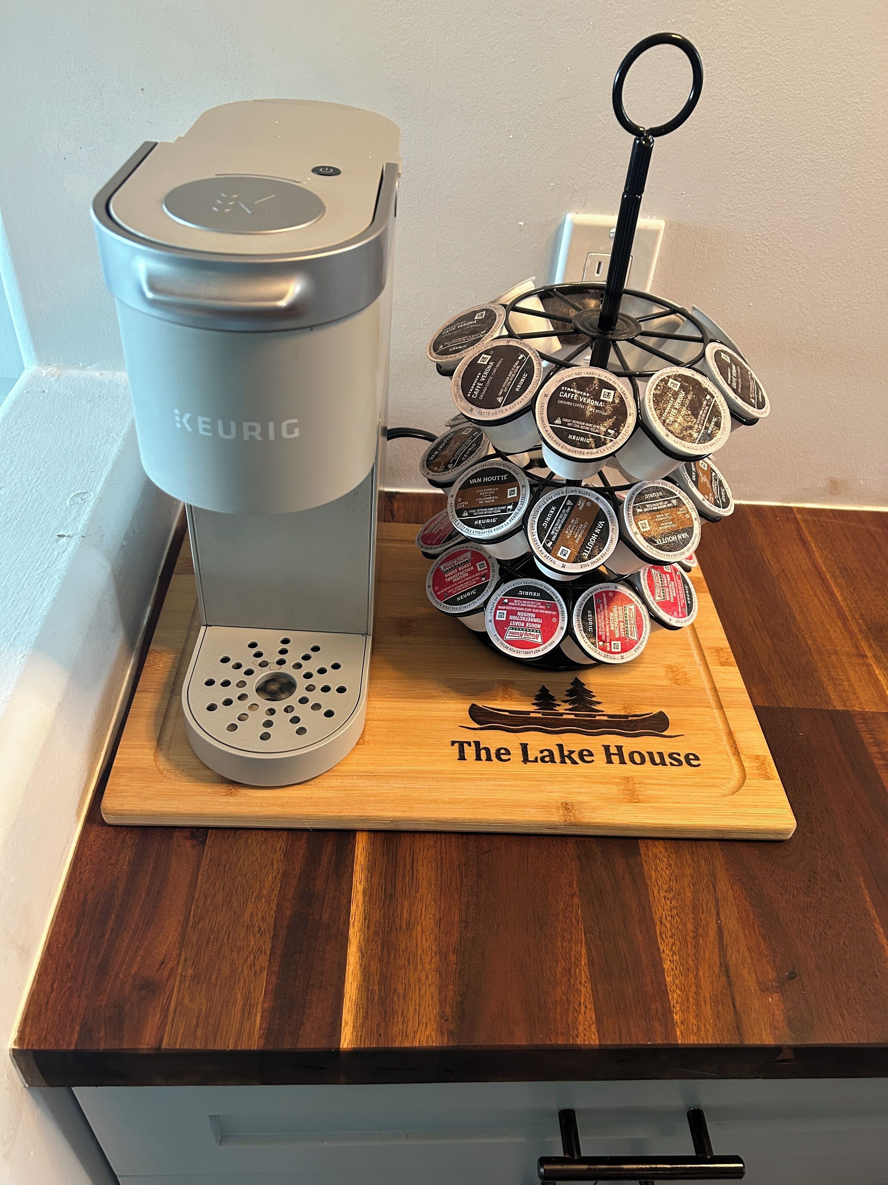 A Keurig coffee maker and a coffee pod holder with a wooden base labeled "The Lake House".