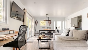 A modern living room with a dining area, large windows, and a minimalist design. - Modern, Sunset-Facing Waterfront Cottage (Yarker)