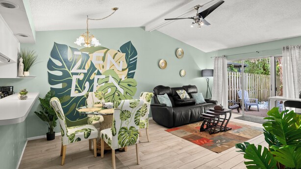 A modern living room with a dining area, a black leather sofa, and a large leafy wall mural. - Pool, Private Yard, Grill, Massage Bed Within 2 miles of USF, Moffit Center (Temple Terrace)