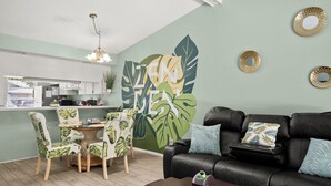 A modern living room with a black leather sofa, a dining table with chairs, and a kitchen area in the background. - Pool, Private Yard, Grill, Massage Bed Within 2 miles of USF, Moffit Center (Temple Terrace)