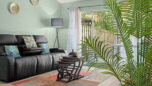 A living room with a black leather sofa, a small table, a floor lamp, and a large plant. - Pool, Private Yard, Grill, Massage Bed Within 2 miles of USF, Moffit Center (Temple Terrace)