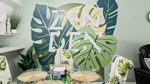 A room with a large tropical leaf mural, a glass table with decorative items, and a black leather chair. - Pool, Private Yard, Grill, Massage Bed Within 2 miles of USF, Moffit Center (Temple Terrace)