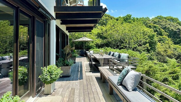 Una terrazza esterna moderna con pavimento in legno, mobili da giardino e vista su un lussureggiante paesaggio.
