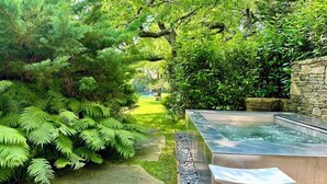 Un giardino tranquillo con una vasca idromassaggio, vegetazione rigogliosa e un muro in pietra.