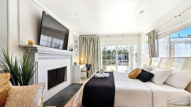 A bedroom with a bed, a television, a fireplace, and a large window. - 7mins LAX/Beach - Gorgeous Home (Hawthorne)