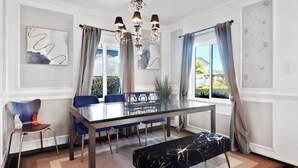 A dining area with a glass table, blue chairs, a bench, and a chandelier. - 7mins LAX/Beach - Gorgeous Home (Hawthorne)
