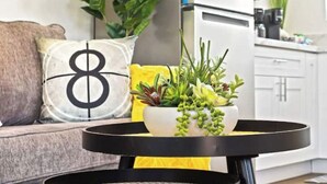 A modern living room with a round black table, a white bowl with plants, a sofa with a cushion featuring the number 8, and a yellow throw blanket. - 7mins LAX/Beach - Gorgeous Home (Hawthorne)