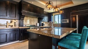 A modern kitchen with dark cabinetry, a granite countertop, and a central island with seating. - Punta Mita Resort (Punta de Mita)