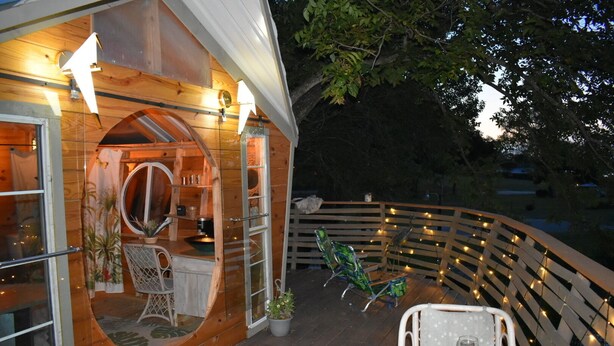 Eine Holzhütte mit einem Rundfenster, einem Essbereich mit Tisch und Stühlen sowie Lichterketten auf der Terrasse.
