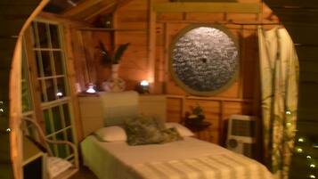 A cozy, circular wooden room with a bed, a small table, and a chair.