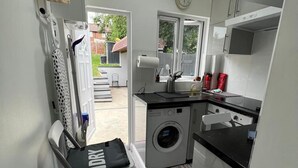 A compact kitchen with a washing machine, a small dining table, and a window overlooking a backyard.