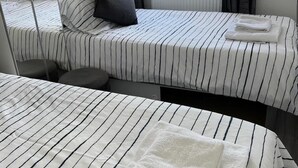 A hotel room with two beds, each with striped bedding and a pillow. There is a window with curtains, a radiator, and a chair.