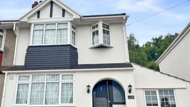 A two-story house with a black front door, white windows, and a small balcony.