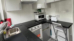 A compact kitchen with grey cabinets, a black countertop, a microwave, a toaster, and a gas stove.