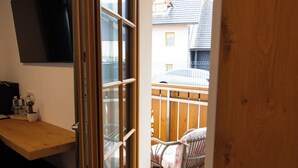 A room with a wooden desk, a television mounted on the wall, and a sliding glass door leading to an outdoor area with a wooden deck and a chair. - Hotel Vila Loka (Skofja Loka)