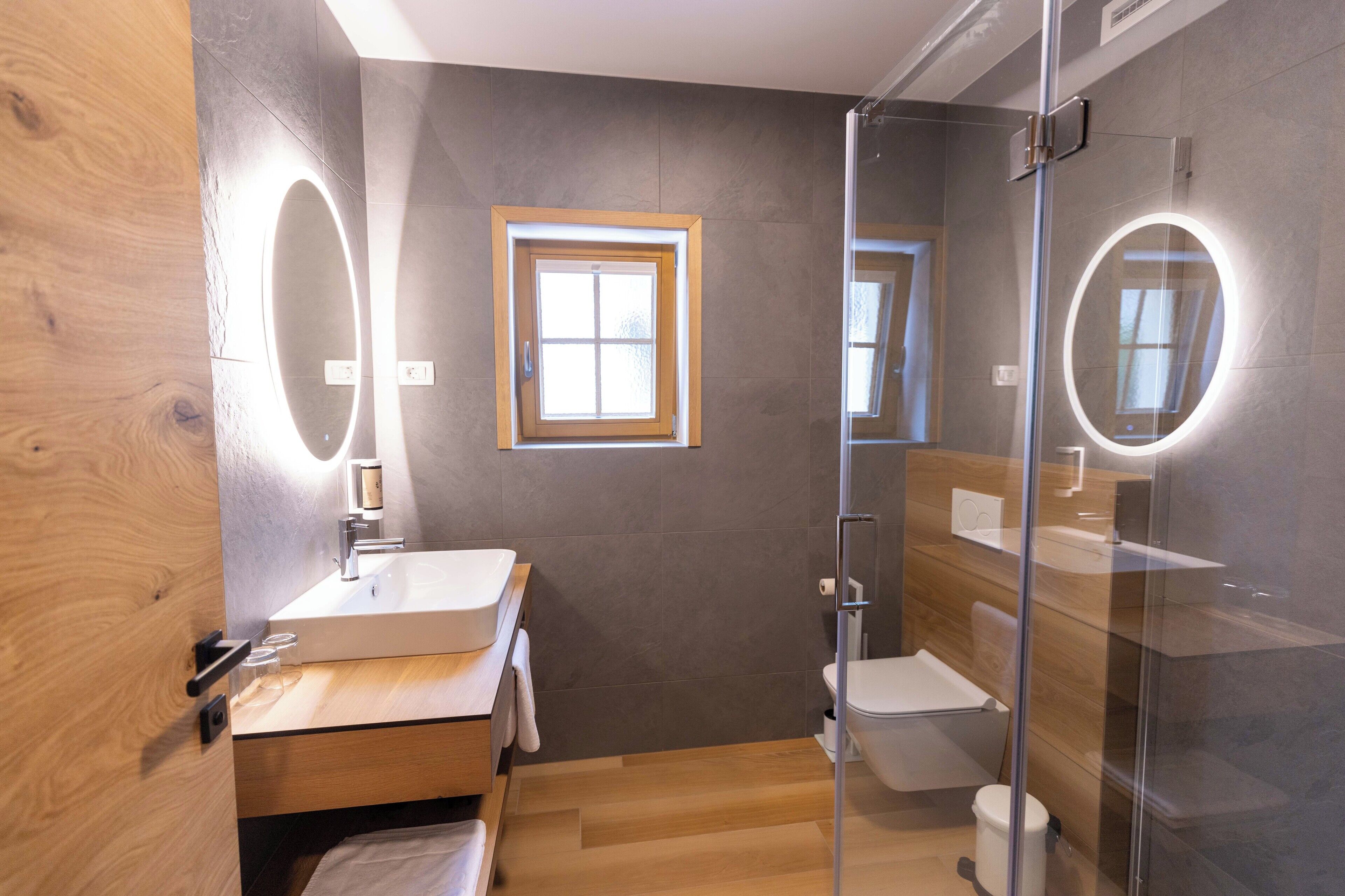 Ein modernes Badezimmer mit einem Holzwaschtisch, einer Duschkabine aus Glas und einem kleinen Fenster.