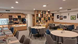 A modern restaurant with round tables and chairs, wooden paneling, and a counter with a display case. - Hotel Vila Loka (Skofja Loka)