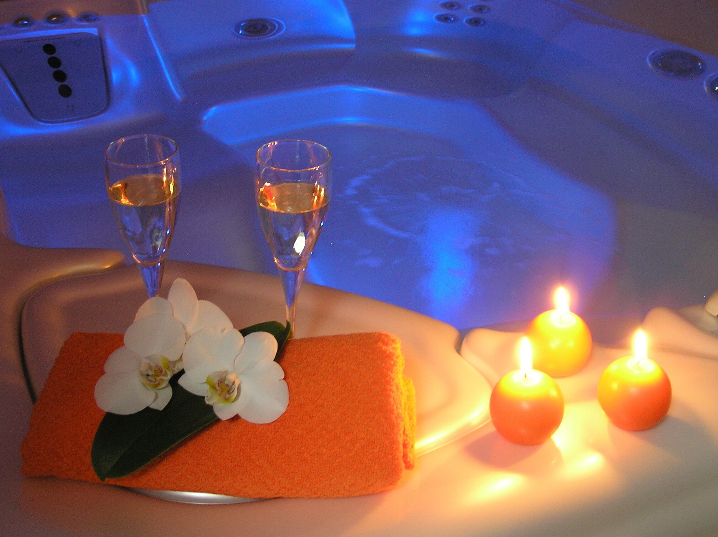 Un décor de spa avec une baignoire, deux verres d’eau, une orchidée et deux bougies allumées.
