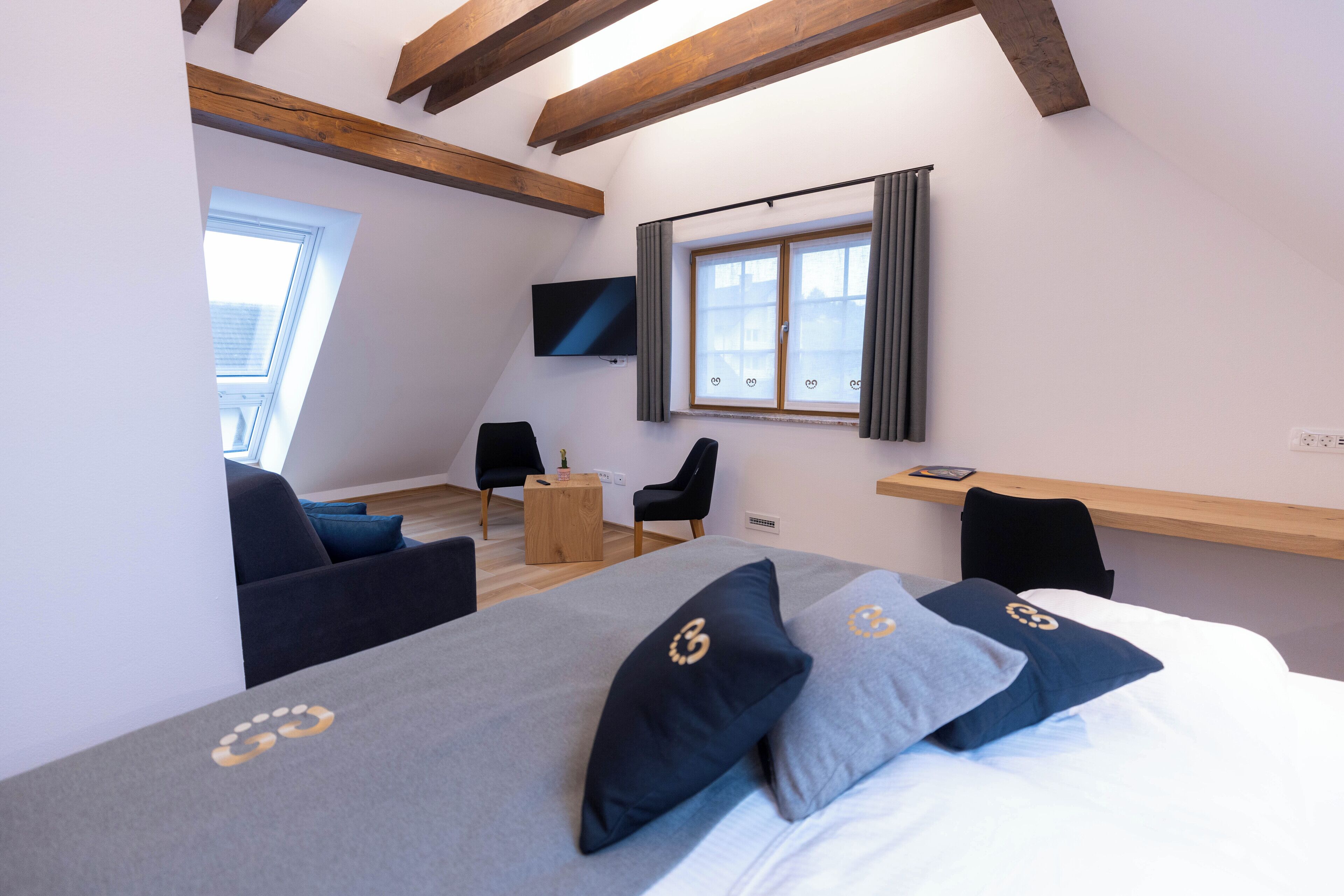 Een moderne hotelkamer met een groot bed, een tv aan de muur, een klein houten tafeltje en een raam met gordijnen.