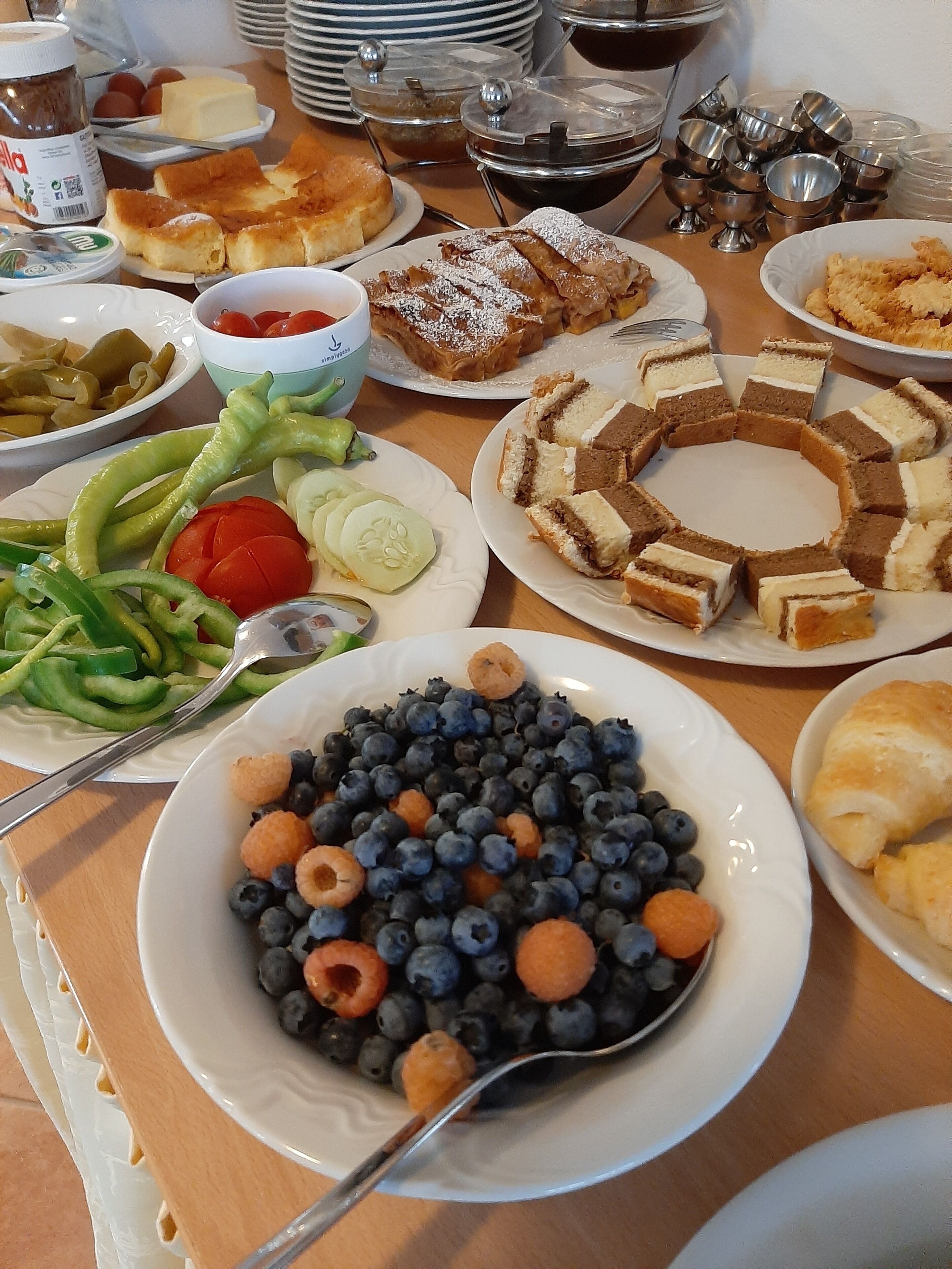 A table with various food items including plates of bread, a bowl of blueberries with raspberries, and some vegetables.
