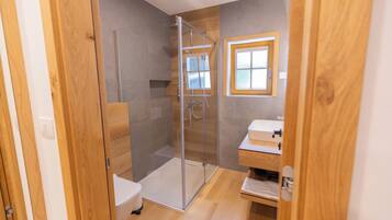 Een moderne badkamer met een glazen douchecabine, een houten wastafelmeubel en een klein raam.